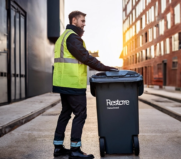 A member of staff ensures data security by holding a secure shredding bin, ready to dispose of sensitive documents in compliance with GDPR and privacy policies.